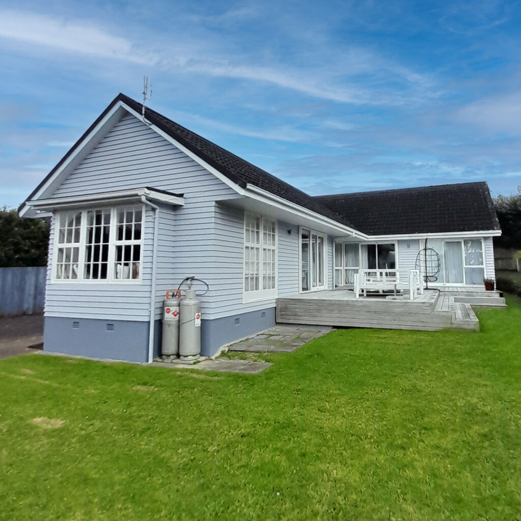 The image features a house with a green lawn, with a house newly painted. The setting includes a clear sky with some clouds in the background.