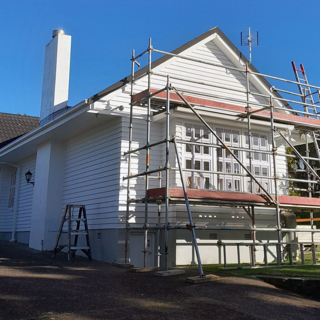 The image is of a house after exterior house painting. It features a cloudy sky, windows, a deck, and is located in Mairangi Bay.