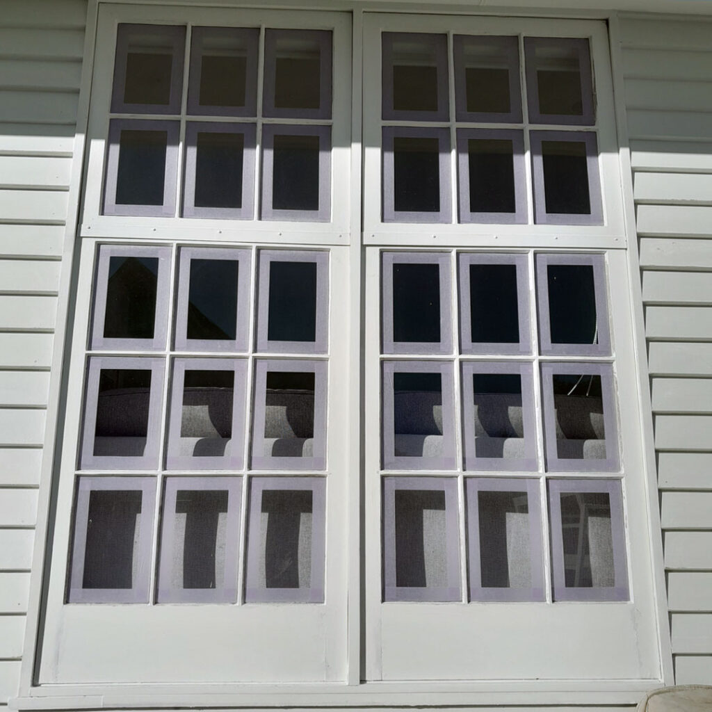 The photo shows a white building with French style windows. The windows appear to be in their original state before painting.