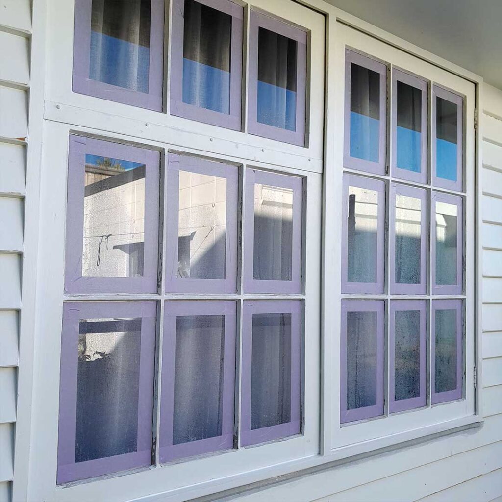 The image depicts a house with windows that are masked ready for exterior house painting.