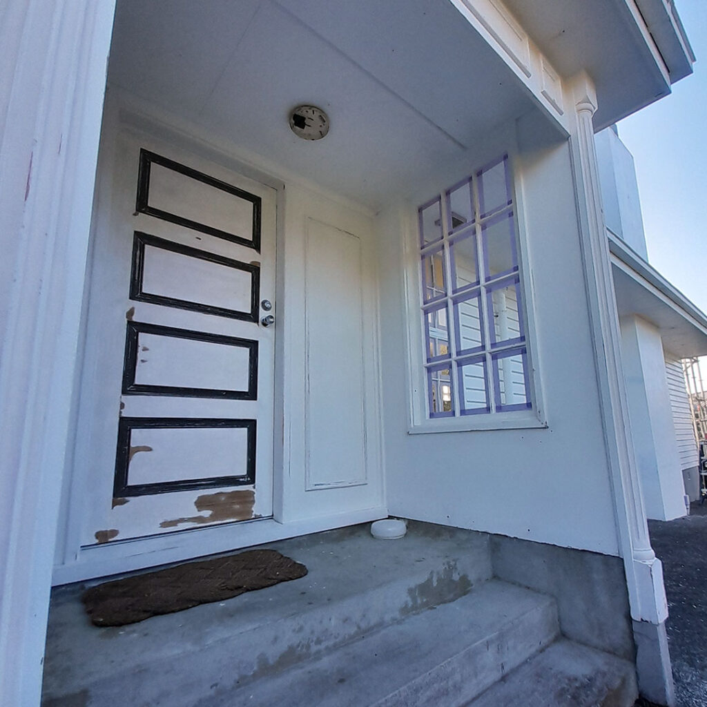 An entrance way with a white door and white windows masked ready for painting