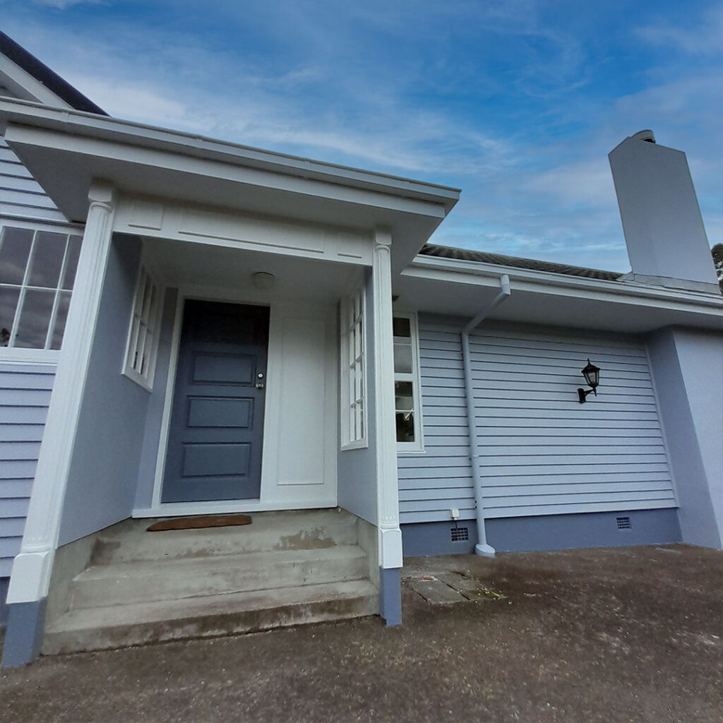 The image is of a white house with grey doors. The house has been painted recently.