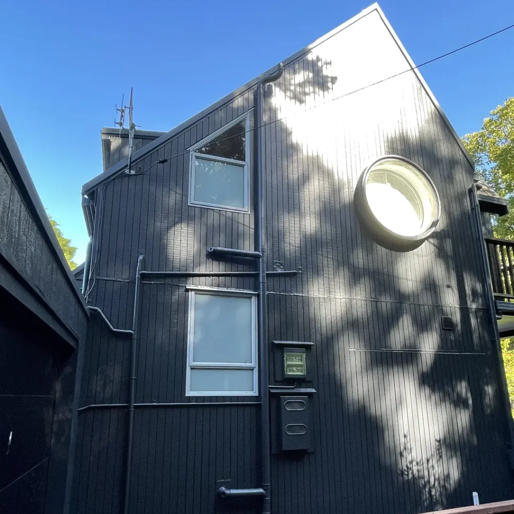 The image depicts a freshly painted house. It features aluminium windows, a roof, vertical cladding, and a distant tree. The house looks new thanks to Weathershield® ColourGuard™ Rawene. paint.