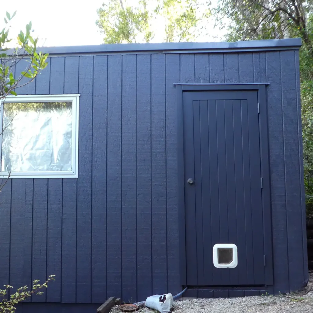 It shows a recently painted shed. It has vertical cladding, aluminium windows, and a far-off tree. Weathershield® ColourGuard™ Rawene. paint has given the house a brand-new appearance.