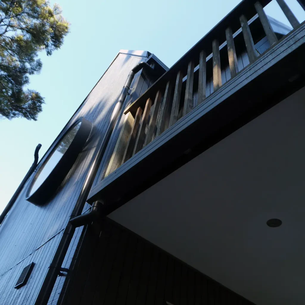 The image is a close-up of a building. It features details such as vertical cladding, soffits, beams, and a round window. The house has been recently painted on the exterior using Weathershield® ColourGuard™ Rawene.