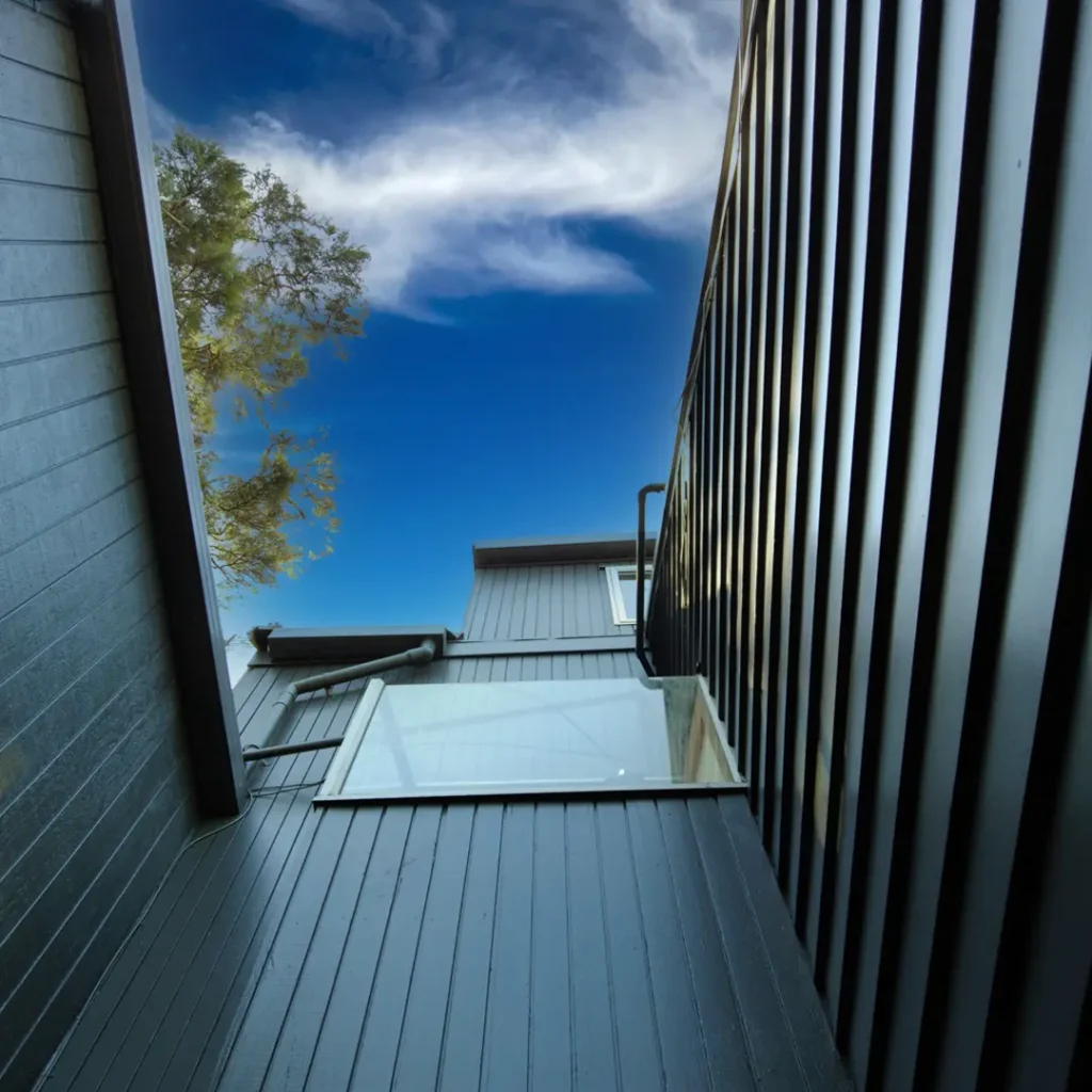 The image shows a building with vertical cladding, under a cloudy sky. The building appears to have aluminium windows and has recently undergone exterior painting using Weathershield® ColourGuard™ Rawene.