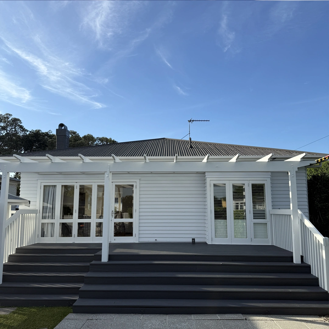 The image showcases a beautifully painted house exterior in Bayswater, Auckland. The fresh coat of paint enhances the home's architectural details, giving it a modern yet timeless appeal. The walls are finished in a smooth, neutral tone, complemented by crisp white trim and window frames that add contrast and elegance. The entrance is inviting, with a well-maintained pathway leading to the door. The surrounding landscaping is neat and well-kept, further enhancing the home’s curb appeal. The flawless paintwork and attention to detail reflect professional craftsmanship, making the house look refreshed and sophisticated.