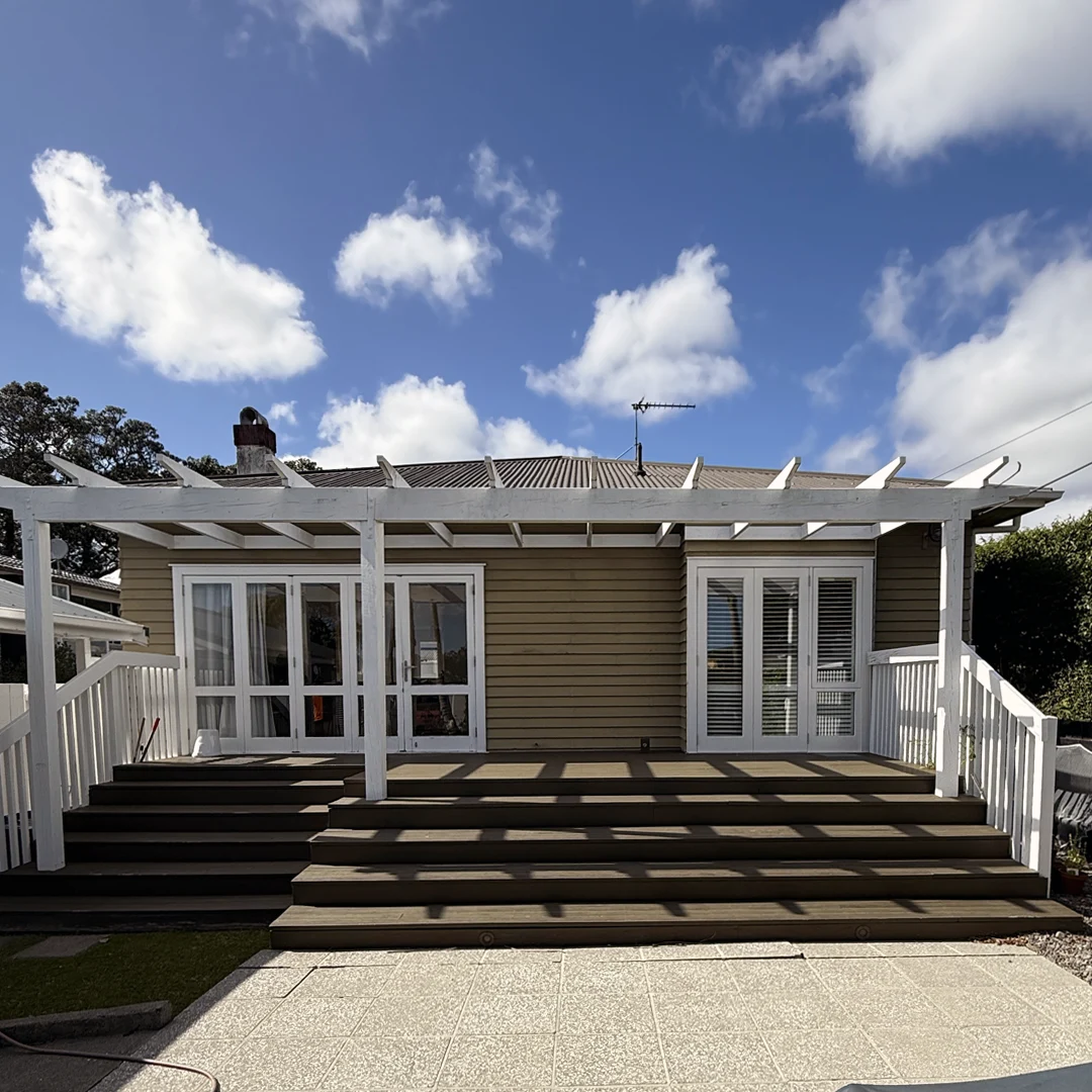 The image showcases a beautifully painted house exterior in Bayswater, Auckland. The fresh paint job gives the home a polished and well-maintained look, enhancing its architectural charm. The walls are finished in a modern, neutral color, complemented by crisp white trim and window frames that add elegance and contrast. The front entrance appears inviting, and the overall aesthetic is clean and sophisticated. The professional craftsmanship is evident in the smooth, even finish, significantly boosting the home's street appeal.